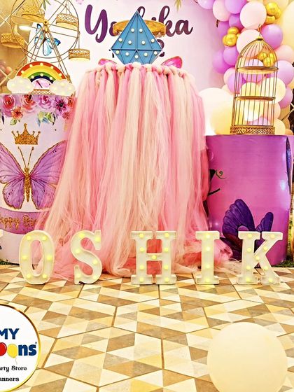 A close-up of a butterfly-themed dessert table, showing the 'YOSHIKA' marquee letters and a tulle-draped plinth.