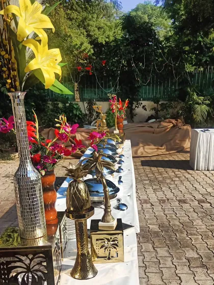 An outdoor catering setup for 80 guests in Vipul Green, Gurgaon. The use of tall, decorative vases with colorful flowers adds height and drama to the buffet line.