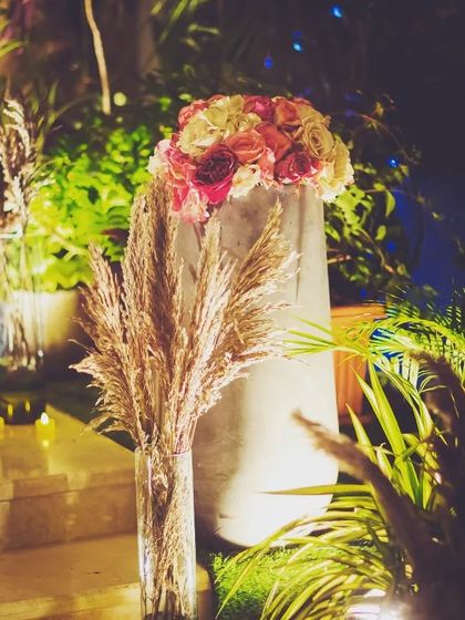An evening view of our modern decor style. A large bouquet of pink and white roses provides a soft, romantic contrast to the rustic pampas grass and concrete-style vase, all bathed in warm light.