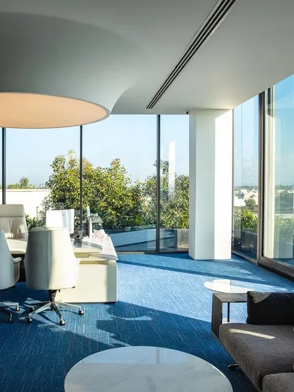Natural light is a key element in my office designs. This executive office is enveloped in floor-to-ceiling glass, offering panoramic views and creating a bright, energizing atmosphere, complemented by a large, modern ceiling light that serves as a functional centerpiece.