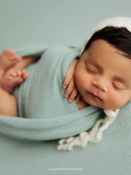 This little one is curled up and cozy, wrapped in a soft blue-green swaddle with a matching white bonnet. This pose is all about comfort and serenity.
