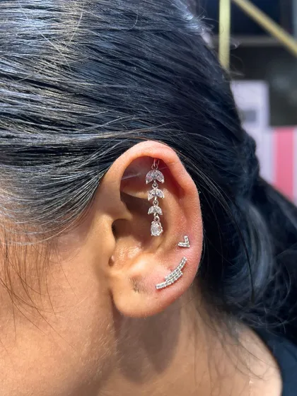 A cascading vine of silver leaves dangles beautifully from this helix piercing, complemented by a simple heart stud and a curved bar.