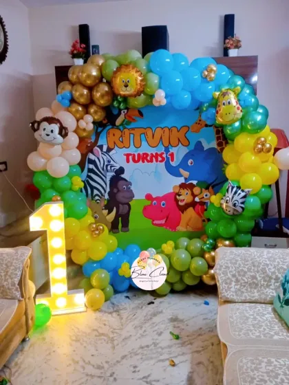 A cute safari animal theme for a first birthday party, complete with a custom backdrop, colorful balloon garland, and a large light-up number '1'.