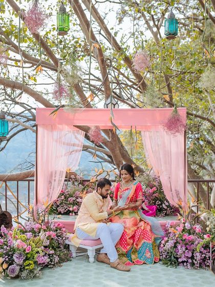 The couple seated on their Mehendi stage, sharing a quiet moment as the groom looks at the bride's henna.