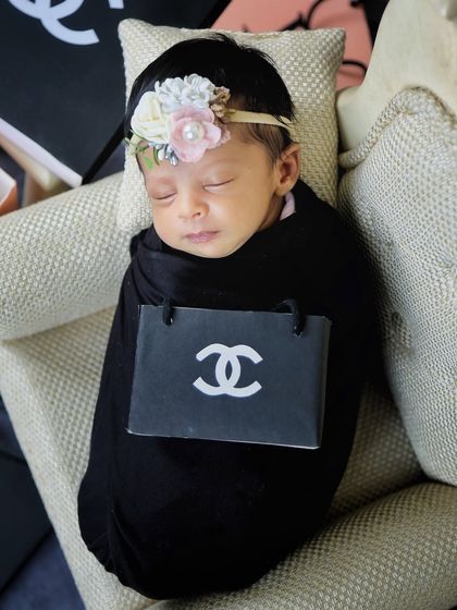 A close-up of our little fashionista, swaddled in black with a miniature Chanel-inspired prop. It's a simple, chic, and playful concept.