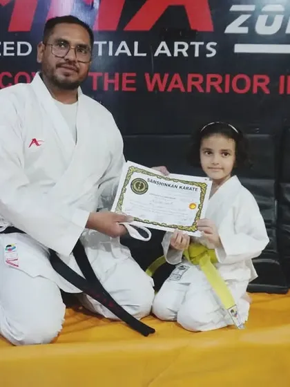 A young girl smiles as she receives her yellow belt and certificate. We foster a positive and encouraging environment for all our students.
