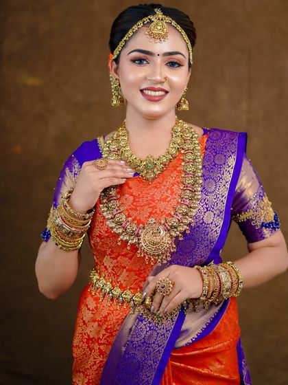 An orange and royal blue Kanchipuram saree styled for a photoshoot. The contrast is striking, and the drape is kept traditional to highlight the saree's grandeur.