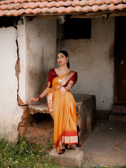 A full-length portrait of a model in a traditional saree, seated on a stone ledge. The rustic setting and her elegant pose create a timeless and beautiful image.