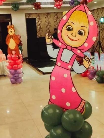 A life-sized Masha cutout on a green balloon base, with the Bear character visible in the background. These props are key to our Masha and the Bear theme.