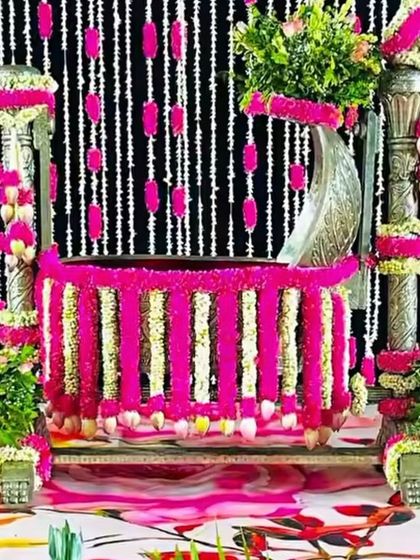 A silver cradle for rent, decorated lavishly with bright pink and white flower garlands against a black and white striped backdrop.