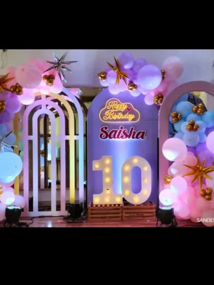 A pretty pastel setup for a 10th birthday party. The decor features arch-shaped backdrops, a light-up marquee number '10', and a "Happy Birthday" neon sign.