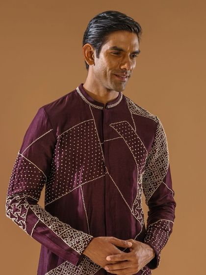 A smiling model wears the deep plum kurta, showcasing the intricate geometric embroidery on the shoulder and sleeve. A perfect piece to add panache to your wardrobe.