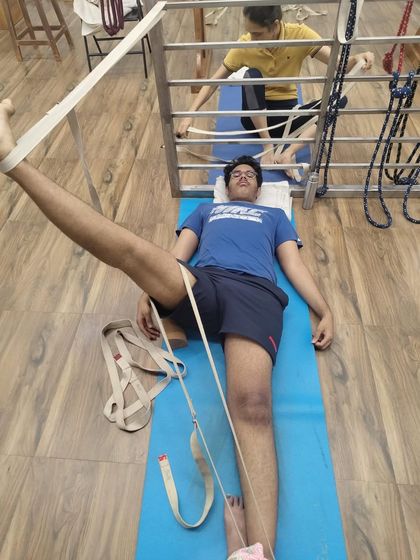 A young student in Supta Padangusthasana using a belt and stall bar for support. This setup helps to isolate the hamstring stretch effectively.