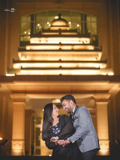 A joyful, candid moment captured against the grand, illuminated architecture of a luxury hotel at night. This image perfectly blends elegance with genuine emotion.