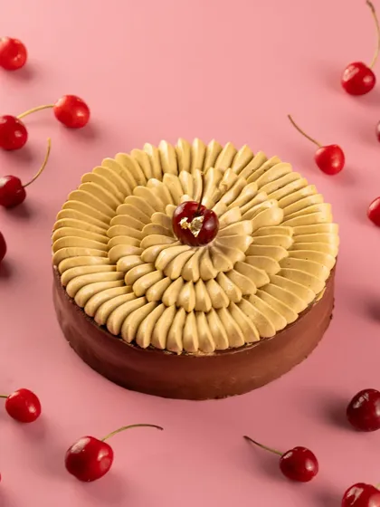 A top-down view of a beautifully piped black forest cake, surrounded by fresh cherries. This is an elegant product shot for a patisserie.