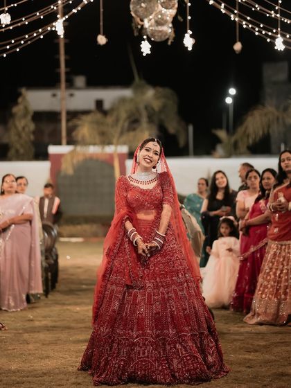 The bride's happy entrance. Her radiant smile as she walks into the event shows her excitement and joy, and her red lehenga looks stunning under the festive lights.