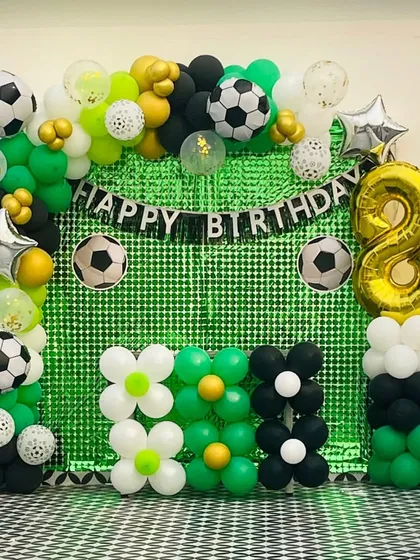 A detailed shot of the football birthday backdrop, showing the 'Happy Birthday' banner, the number '8' foil balloon, and flower-shaped balloon arrangements at the base.