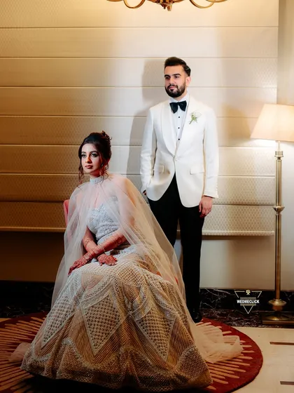 A regal and posed portrait of the couple, the bride seated and the groom standing, exuding timeless elegance.