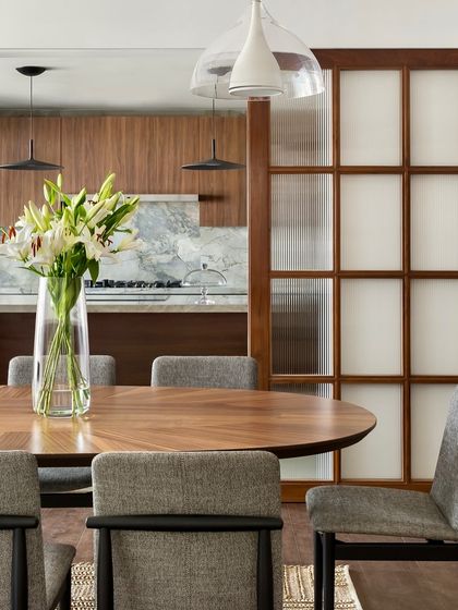 A close-up of the dining table in the West Coast Residence, where a simple vase of lilies adds a touch of natural beauty. The view extends into the kitchen, highlighting the open yet layered design.