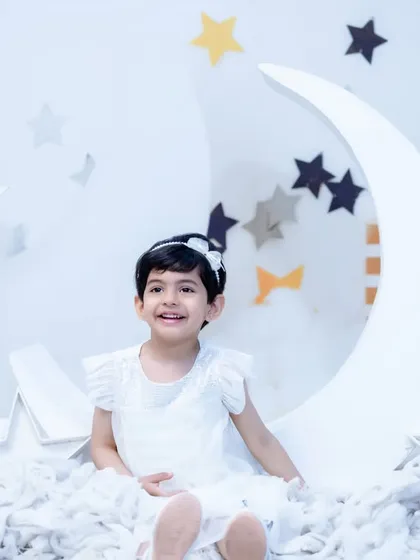 A joyful girl in a simple white dress, smiling brightly in our white and grey moon and stars setup. A timeless and happy birthday photo.