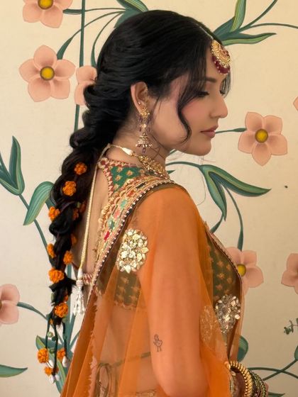 A side profile of a bride with her hair in a loose, romantic braid decorated with marigold flowers for her Mehandi.
