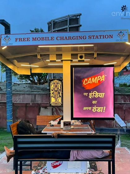 A man rests on the bench of our solar hut in Ayodhya, demonstrating the practical utility and comfort our installations provide to the public. The structure offers shelter while his device charges, creating a positive user experience.