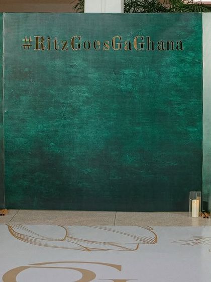 A modern, minimalist photo backdrop for the Sangeet, featuring a textured green wall with the couple's custom wedding hashtag.