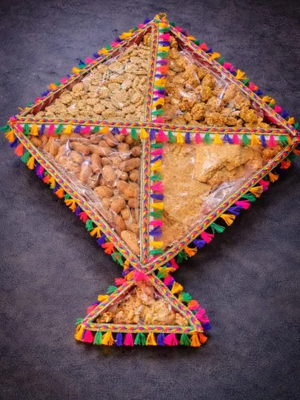 A unique kite-shaped Lohri platter, divided into sections and filled with peanuts, gajak, and other traditional treats. The colorful tassel border makes it extra festive.