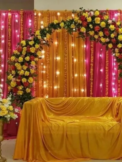 A classic Haldi stage for a home event. The combination of yellow and pink drapes with a floral arch and fairy lights creates a warm and inviting look.