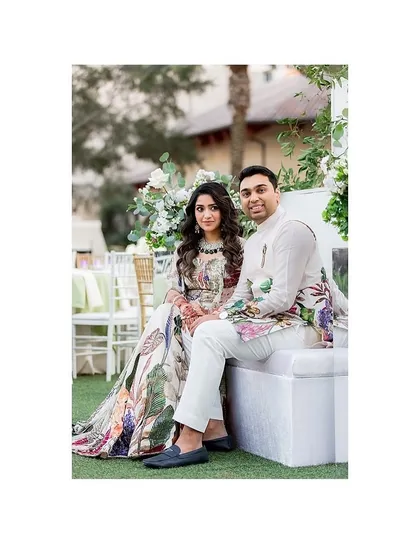 A seated portrait of the couple at their Sangeet. The intricate floral prints on their outfits are beautifully detailed, creating a look of timeless elegance.