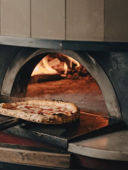 A moody shot of a pizza baking away in the wood-fired oven. The glow of the fire is what gives our pies their unique, smoky flavour.