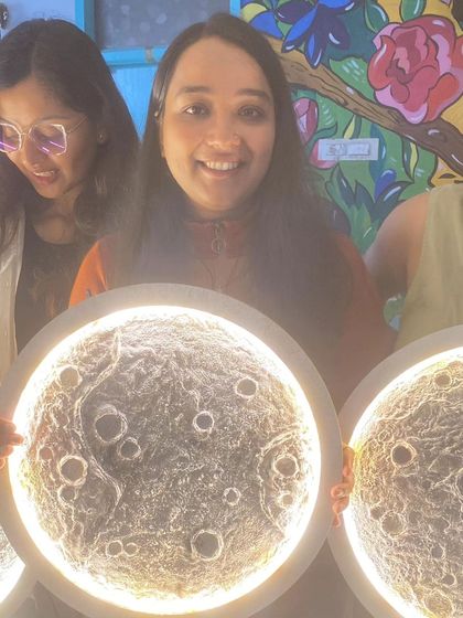 The joy of creation is evident on this participant's face as she displays her handmade 3-D moon lamp against our colorful café mural.