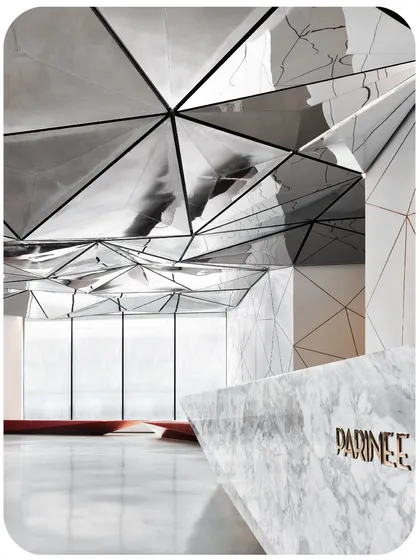 A close-up of the faceted marble reception desk, showing the PARINEE logo with its rose-gold inlay. This detail highlights the project's emphasis on high-quality materials and craftsmanship.