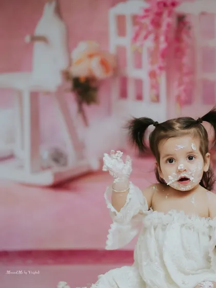 Reaching out with a hand full of frosting. The soft pink tones and her joyful expression make this a beautiful memory.