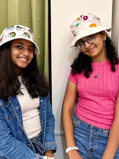 Two friends posing with their stylish, custom-painted bucket hats. It's a great bonding activity for a birthday party.
