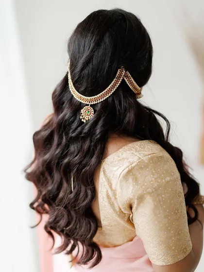Hairstyling is just as important as makeup. This image details a traditional South Indian hairstyle with soft, open curls, elegantly accessorized with a statement hairpiece. This style is perfect for adding a touch of royalty to a saree look for any special occasion.
