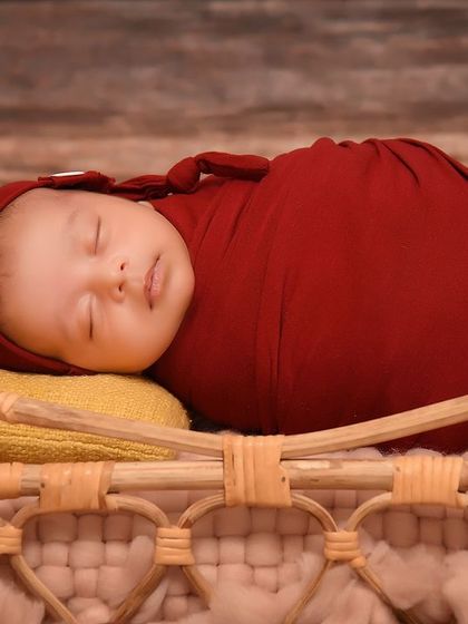 A close-up of a baby in a red wrap, part of a Snow White inspired theme with red apples and a rustic wooden bed.