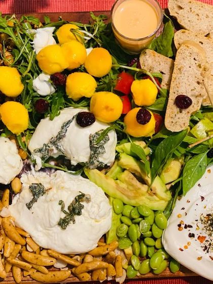 A stunning fresh cheese platter featuring burrata and other soft cheeses, surrounded by apricots, roasted chickpeas, avocado, and fresh bread.