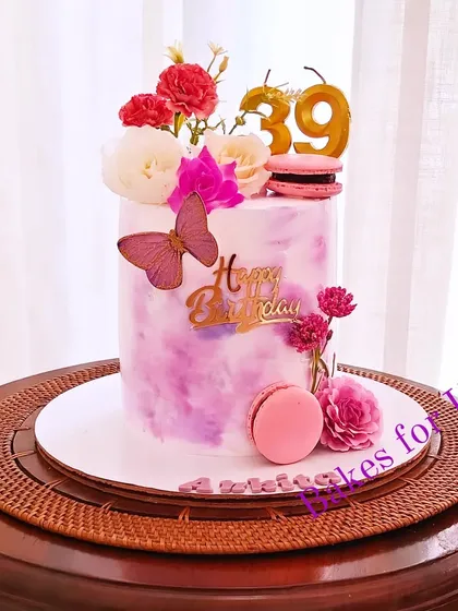 A tall cake with a purple watercolor finish, decorated with fresh flowers, macarons, and a butterfly accent. A beautiful and chic design for a 39th birthday.