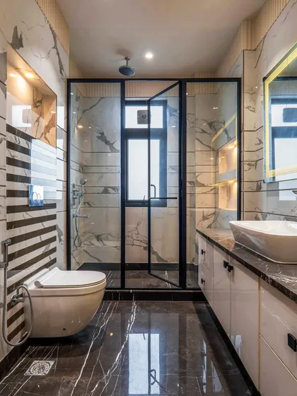In this bathroom, I combined striped wall tiles with a marble-patterned wall for a dynamic effect. The black-framed shower enclosure and dark flooring ground the space and add a modern edge.