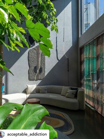 A close-up view of a living area adjacent to an indoor courtyard. The leaves of the tree frame the shot, highlighting the seamless integration of the plant life with the interior decor and art.