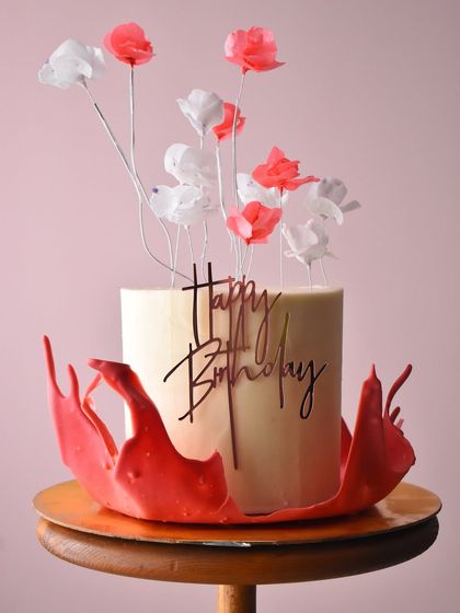 An artistic and modern birthday cake. This design features delicate, handcrafted wafer paper flowers and a dramatic red chocolate sail, creating a beautiful contrast of textures and colors.