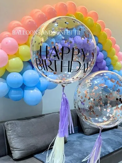 Personalized confetti and 'Happy Birthday' bubble balloons add a special touch to the rainbow-themed decor.