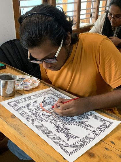 The student is deeply focused on his Madhubani artwork, carefully filling in the colors. This is where tradition is passed on to the next generation.