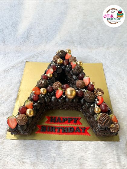 A personalized monogram cake for a birthday celebration. This letter 'A' cake is made from rich chocolate cake and decorated with fresh fruits, Ferrero Rocher, and gold spheres.