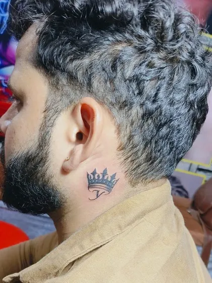 Even small tattoos require great precision. This is a crown tattoo with an initial 'J' placed just behind the ear, a popular spot for a discreet yet stylish design.
