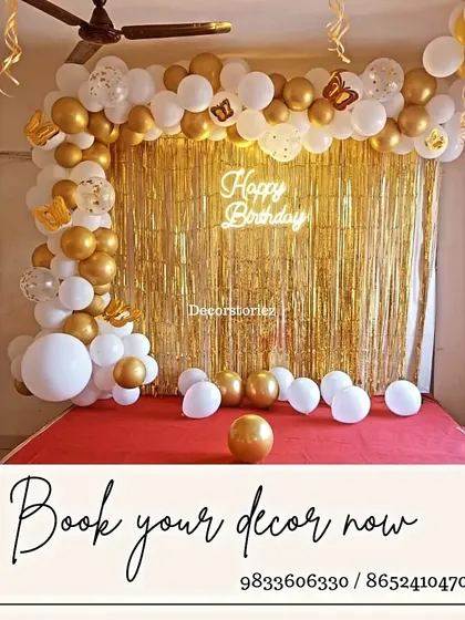 A classic and elegant birthday backdrop with a white and gold balloon arch over a gold fringe curtain, completed with a 'Happy Birthday' neon sign.