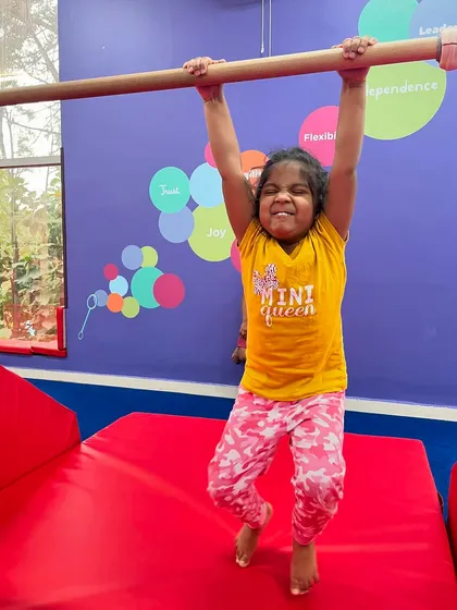 With a look of pure effort, this young girl hangs from the bar, building her strength and resilience. Each attempt, successful or not, is a step towards becoming a more confident athlete.