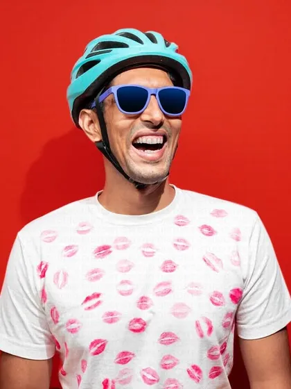This lifestyle shot for a sunglasses brand is full of energy and personality. The bright red background, fun t-shirt, and the model's joyful expression create a vibrant and youthful image.