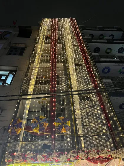 This is how I turn a building into a 'shadi wala ghar'. The entire facade is draped in red and white fabric with vertical streams of fairy lights, creating a grand and festive announcement of the wedding celebrations within.